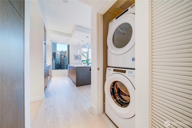 laundry area with laundry area, baseboards, stacked washer / dryer, a city view, and light wood-style floors