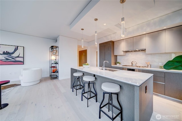 kitchen with a sink, a kitchen breakfast bar, light wood finished floors, modern cabinets, and tasteful backsplash