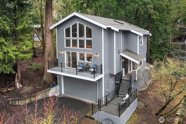 exterior space with a garage, driveway, stairway, roof with shingles, and a view of trees