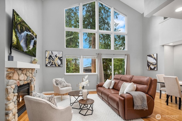 living room featuring light wood-type flooring, a fireplace, a towering ceiling, and baseboards