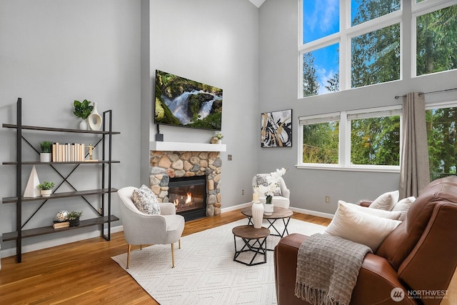 living area featuring a fireplace, a towering ceiling, baseboards, and wood finished floors