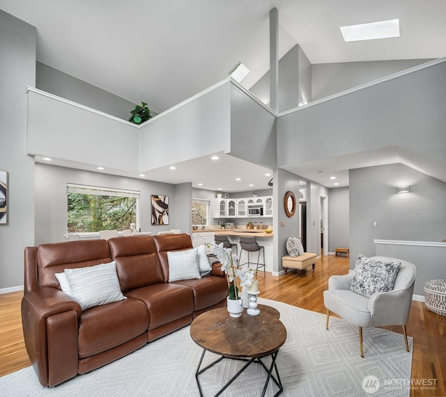 living room featuring a skylight, baseboards, wood finished floors, high vaulted ceiling, and recessed lighting