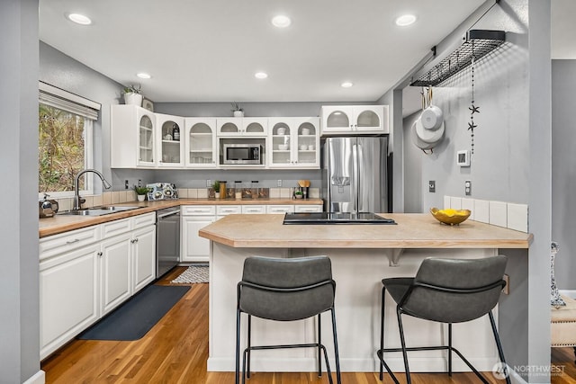 kitchen with a breakfast bar area, appliances with stainless steel finishes, white cabinets, a sink, and a peninsula