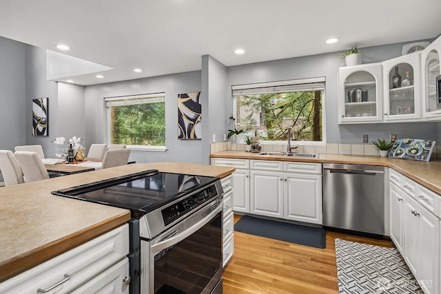 kitchen featuring stainless steel appliances, light wood-style flooring, glass insert cabinets, white cabinets, and a sink