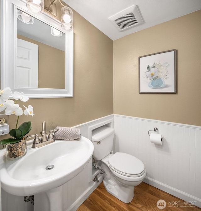 half bathroom with visible vents, toilet, wainscoting, a sink, and wood finished floors