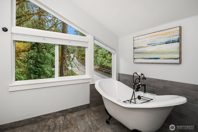 full bathroom with a wainscoted wall, vaulted ceiling, a soaking tub, and tile walls