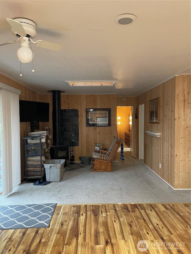 unfurnished living room featuring a ceiling fan, a wood stove, wood walls, and wood finished floors