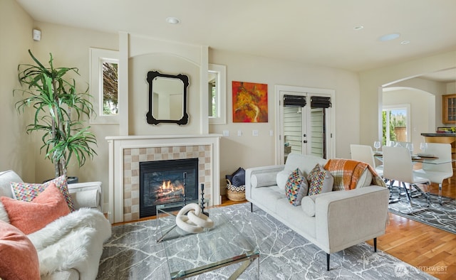 living area with arched walkways, wood finished floors, and a tiled fireplace