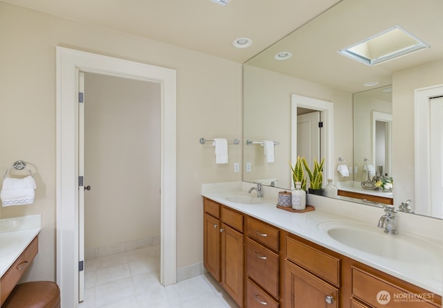 full bath with double vanity, a skylight, baseboards, and a sink