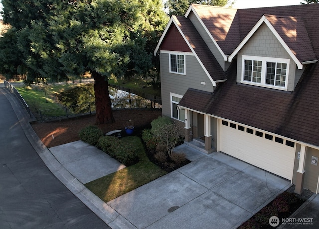 view of front facade featuring a shingled roof, concrete driveway, an attached garage, and fence