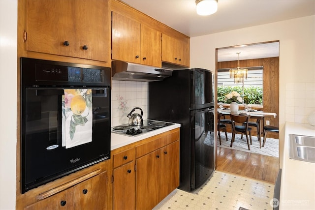 kitchen featuring light floors, light countertops, hanging light fixtures, under cabinet range hood, and black appliances