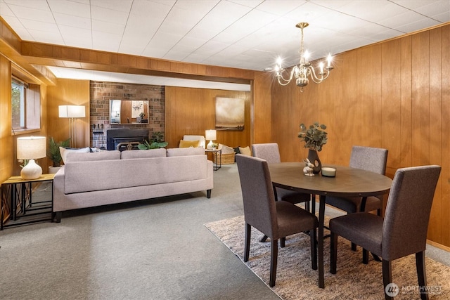 carpeted dining area with wood walls, a fireplace, and an inviting chandelier