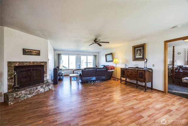 living area with light wood-style floors, a premium fireplace, baseboards, and a ceiling fan