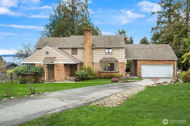 traditional-style home featuring a garage, a chimney, aphalt driveway, a front lawn, and brick siding