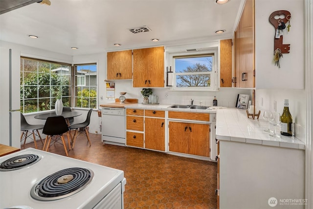 kitchen with brown cabinets, white appliances, visible vents, and a sink