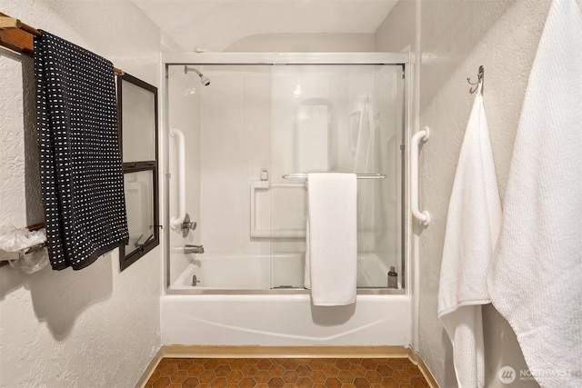 full bath featuring baseboards, bath / shower combo with glass door, and a textured wall