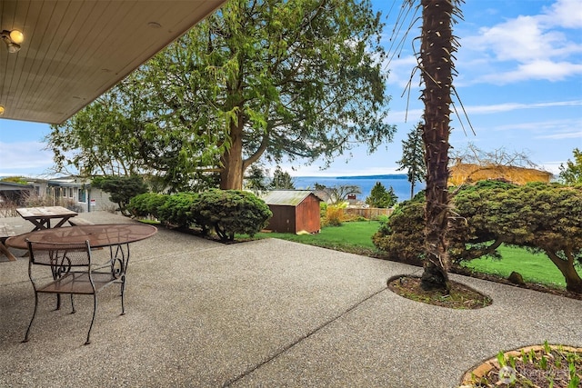 view of patio with a water view, outdoor dining space, a shed, and an outbuilding