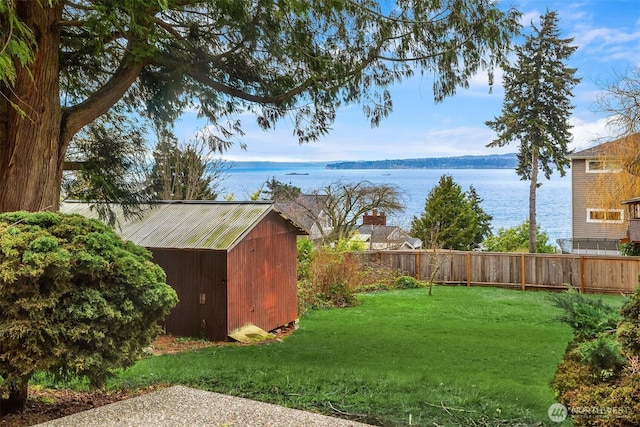 view of yard featuring a storage shed, a water view, fence, and an outdoor structure