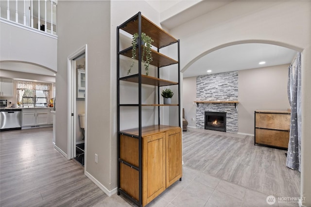 living area with light wood-type flooring, a fireplace, arched walkways, and baseboards