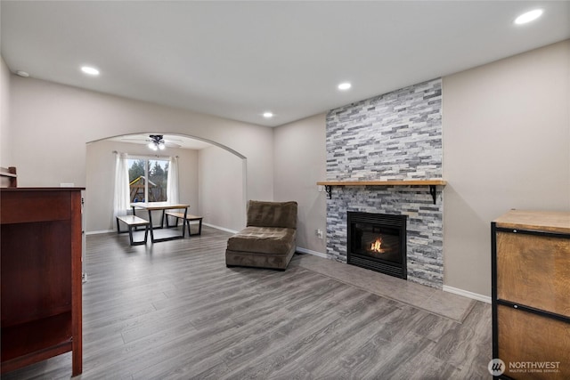 sitting room with arched walkways, recessed lighting, a fireplace, wood finished floors, and baseboards