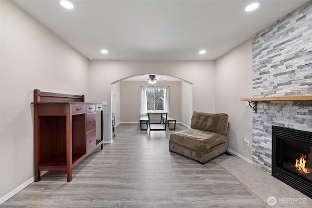 living area featuring arched walkways, recessed lighting, a stone fireplace, wood finished floors, and baseboards