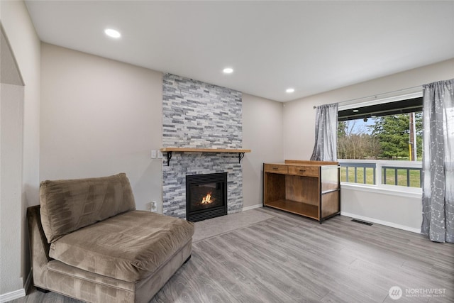 sitting room with a stone fireplace, wood finished floors, visible vents, and baseboards