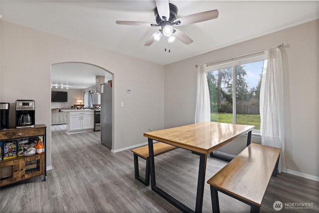 dining room featuring arched walkways, ceiling fan, wood finished floors, and baseboards