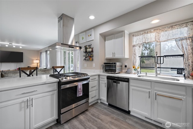 kitchen with visible vents, white cabinets, appliances with stainless steel finishes, a peninsula, and island exhaust hood