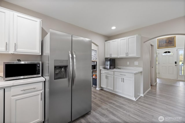 kitchen featuring light wood-type flooring, arched walkways, stainless steel appliances, and light countertops