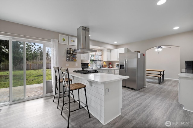 kitchen featuring a peninsula, light wood-style floors, light countertops, stainless steel fridge with ice dispenser, and island exhaust hood