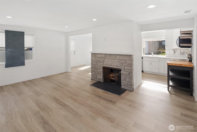 unfurnished living room featuring baseboards, light wood-type flooring, a fireplace, a sink, and recessed lighting