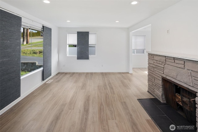 unfurnished living room with a stone fireplace, recessed lighting, light wood-style flooring, and baseboards