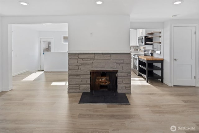 living area with recessed lighting, a stone fireplace, light wood-style flooring, and baseboards