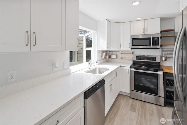 kitchen featuring white cabinets, light wood finished floors, stainless steel appliances, and a sink