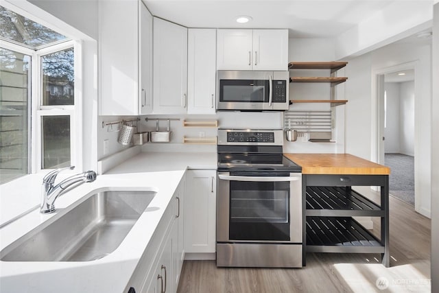 kitchen featuring stainless steel appliances, light wood-style flooring, a sink, and white cabinetry