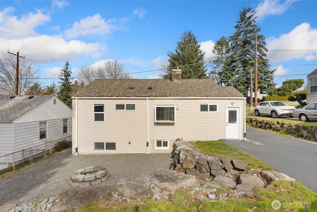 rear view of property with a shingled roof, a chimney, fence, and a fire pit