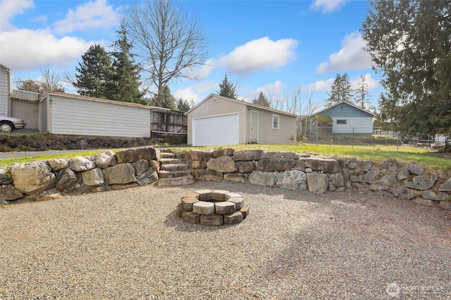 exterior space featuring a detached garage, fence, a fire pit, and an outdoor structure