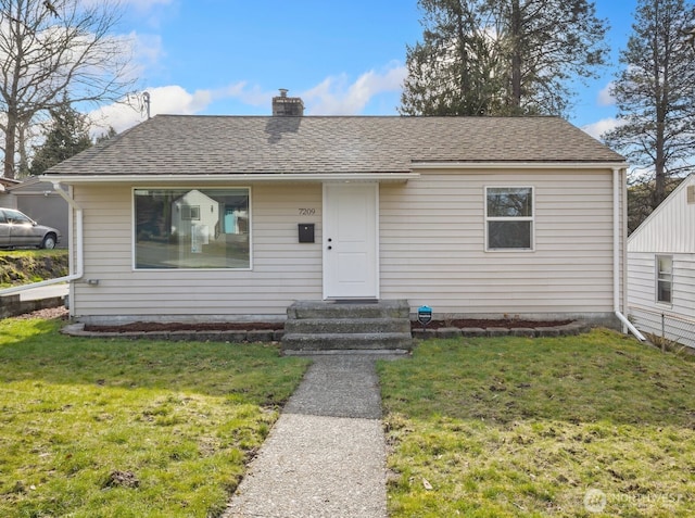 view of front of home with roof with shingles, a chimney, and a front yard