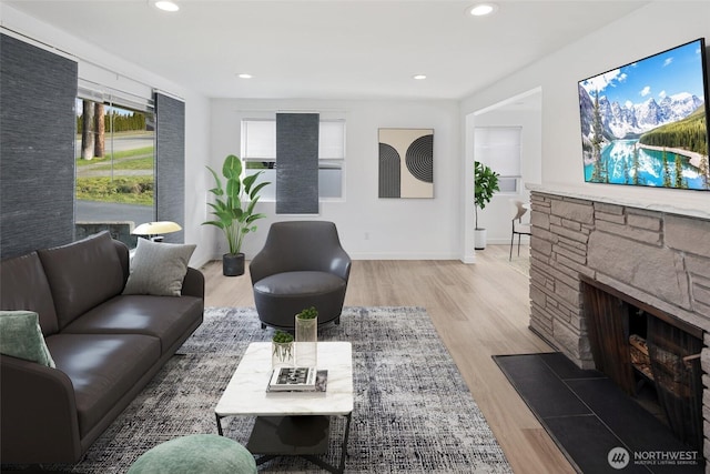 living room with baseboards, a stone fireplace, recessed lighting, and light wood-style floors