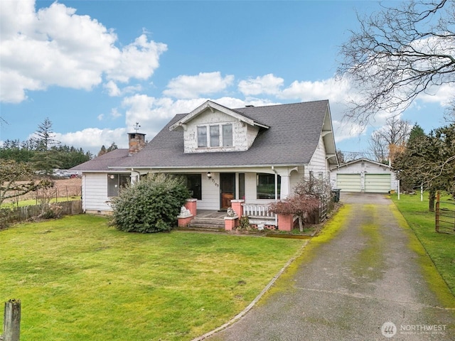 bungalow featuring a shingled roof, a porch, an outbuilding, fence, and a front lawn