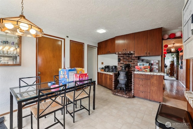 kitchen with a textured wall, brown cabinets, hanging light fixtures, light countertops, and a textured ceiling