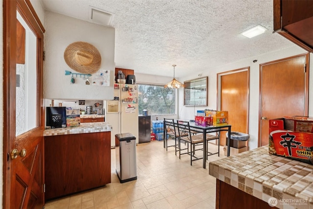 kitchen with white fridge with ice dispenser, tile counters, a textured ceiling, and decorative light fixtures