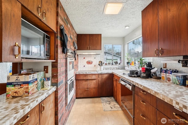 kitchen with dishwasher, brown cabinets, light countertops, a textured ceiling, and black microwave