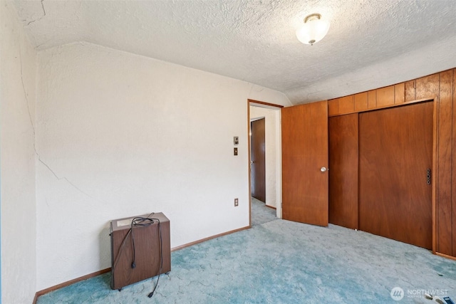 unfurnished bedroom featuring vaulted ceiling, carpet floors, a textured ceiling, and baseboards