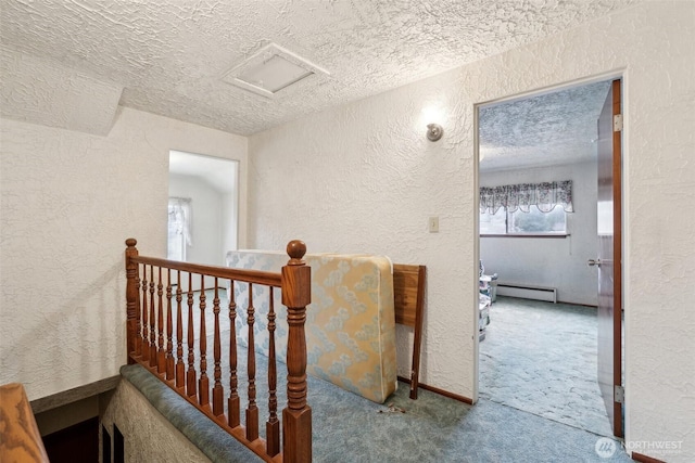 hallway with a textured ceiling, a textured wall, carpet floors, and attic access