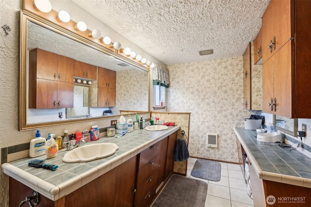 bathroom with double vanity, a sink, a textured ceiling, tile patterned flooring, and wallpapered walls