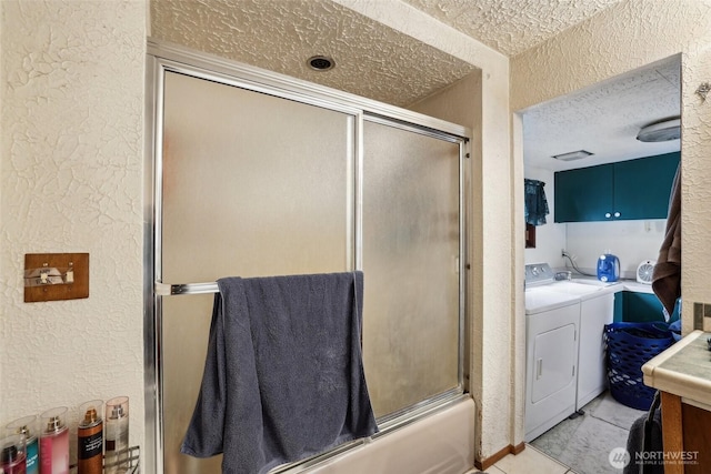 bathroom featuring a textured ceiling, a textured wall, combined bath / shower with glass door, and washer and clothes dryer