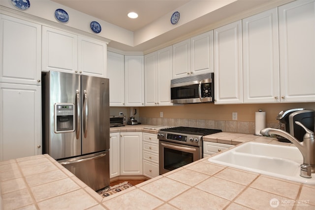 kitchen featuring tile countertops, recessed lighting, stainless steel appliances, a sink, and white cabinetry