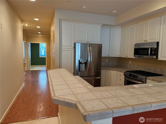 kitchen with stainless steel appliances, tile counters, recessed lighting, wood finished floors, and baseboards