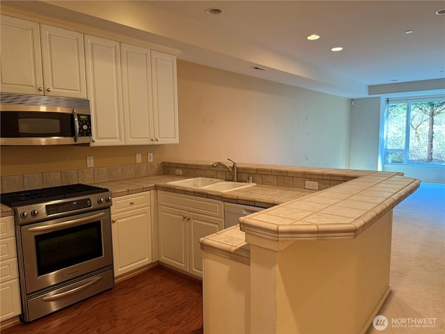 kitchen featuring a peninsula, white cabinetry, appliances with stainless steel finishes, and tile counters